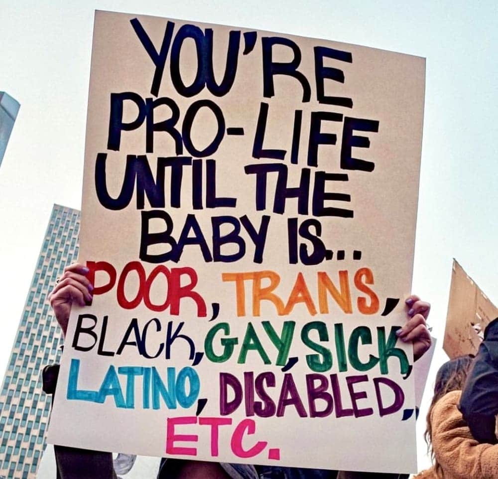 abortion and women's rights activist holds up a sign that says you're pro-life until the baby is poor, trans, black, gay, sick, latino, disabled etc
